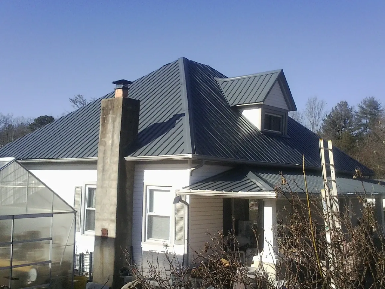 Dark blue standing seam metal roof on a white farmhouse with dormer — Slate & Tile Roof Repair by Roofing Brothers in Carlock