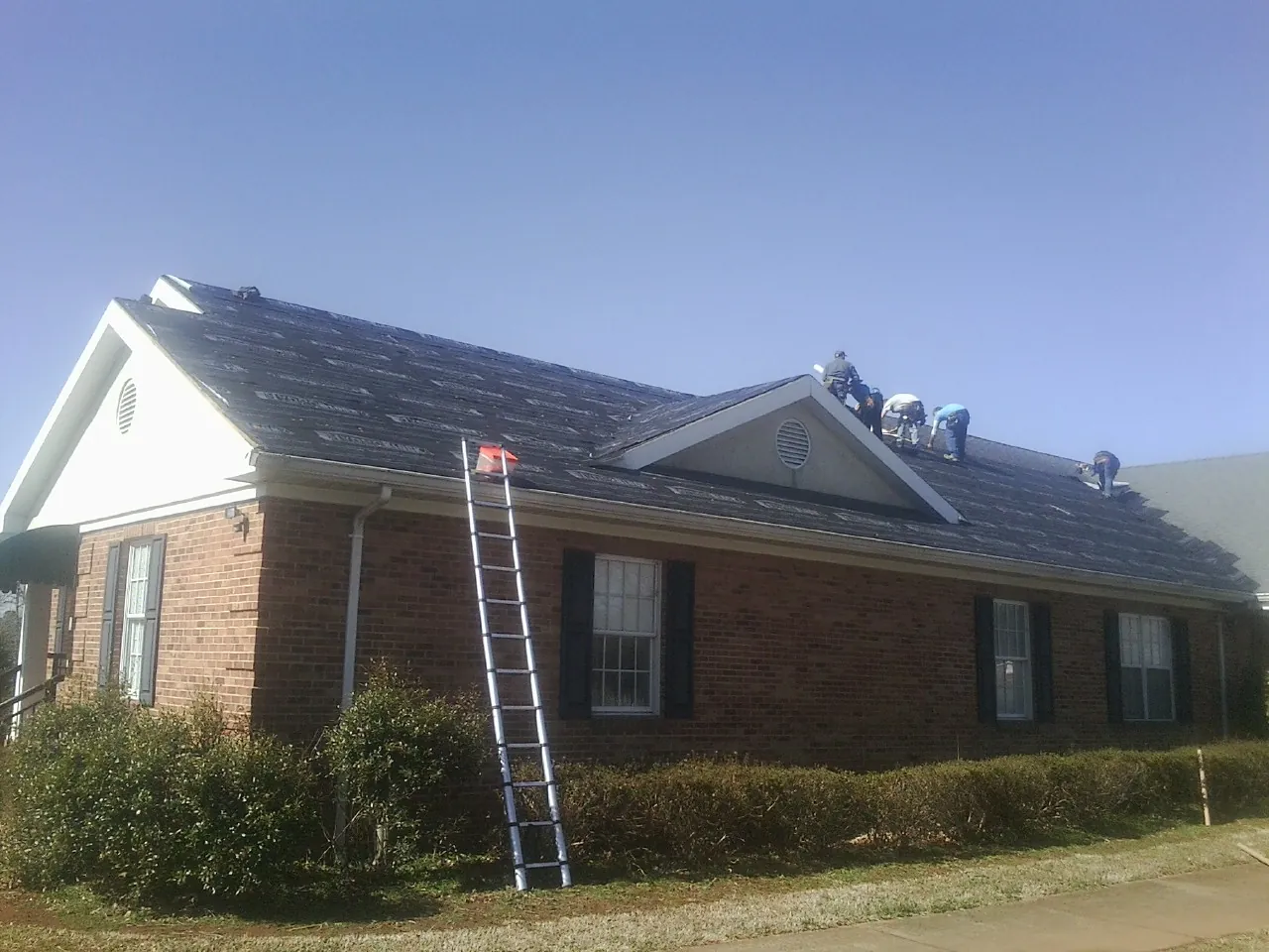 Crew tearing shingles off a brick ranch roof with a ladder set — Metal Roof Repair work by our crew in Carlock