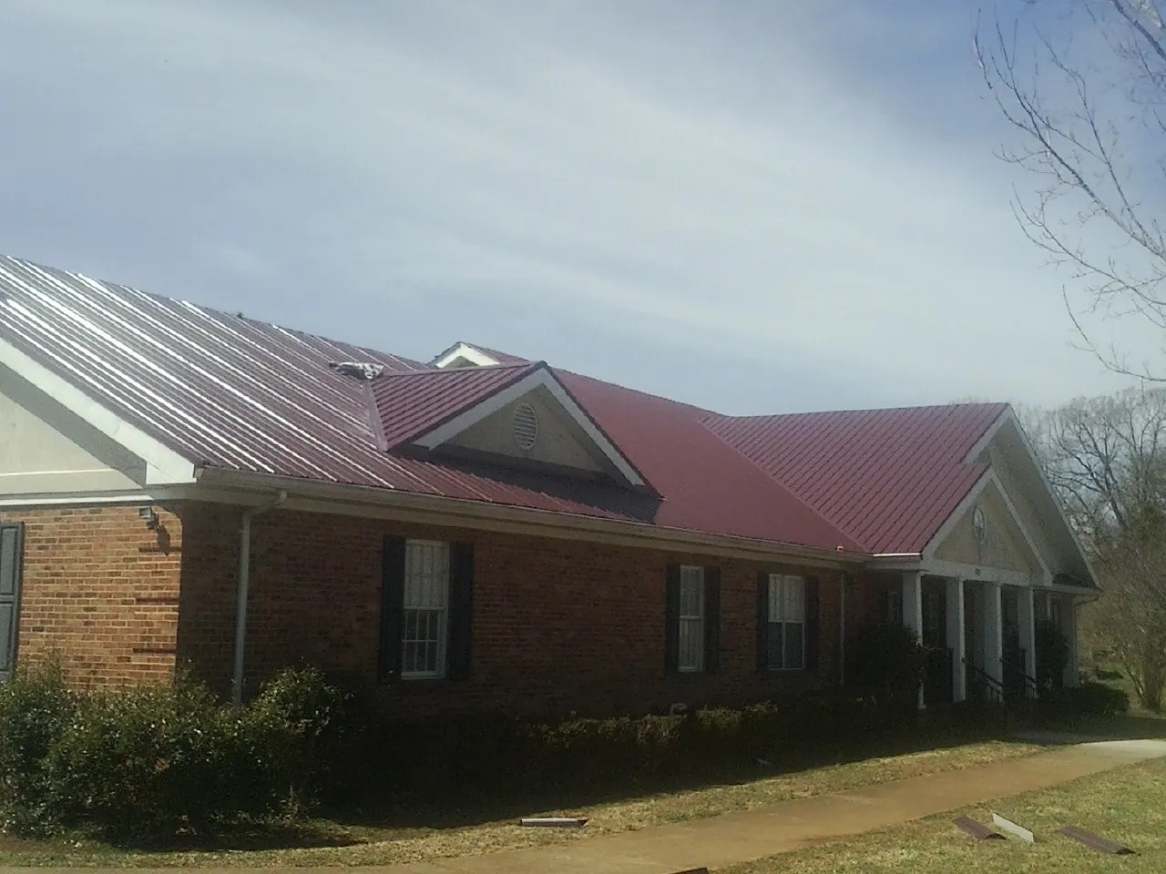Red metal roof with gabled entries on a long brick building, from a Hail Damage Roof Repair job in Carlock