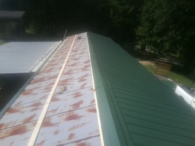 Old rusted panels beside newly installed green metal roofing — Wind Damage Roof Repair by Roofing Brothers in Carlock