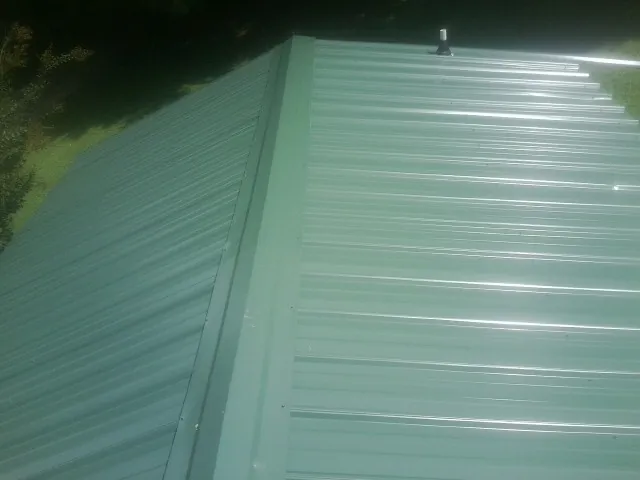 New green metal panels meeting at the ridge of a roof — Flat Roof Repair work by our crew in Carlock
