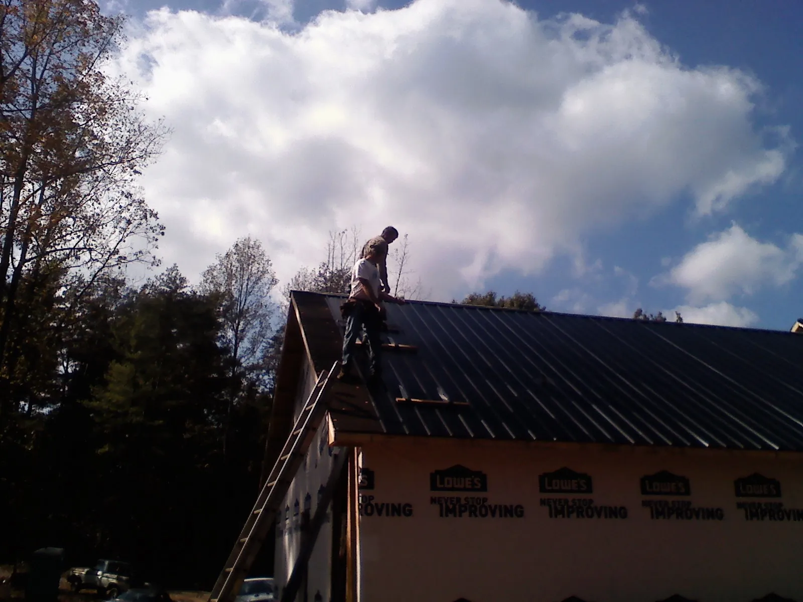 Roofer fastening dark metal panels high against a cloudy sky, from a Roof Inspection job in Carlock